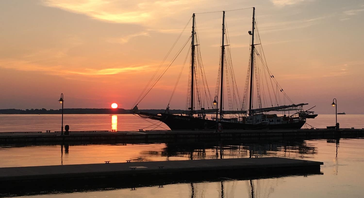Large sailboat tied to a dock with the setting sun in the background