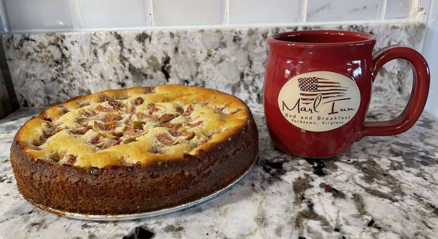 Close up view of a homemade coffee cake and red stoneware cup with Marl Inn logo on it