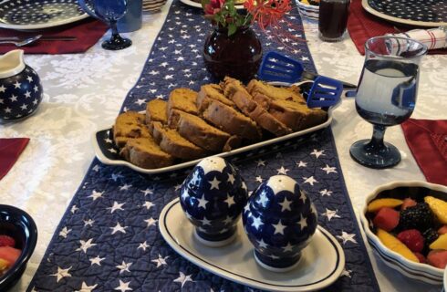 Close up view of a table decorated with red, white, and blue patriotic place settings, table runner, and dishes with fruit and coffee cake