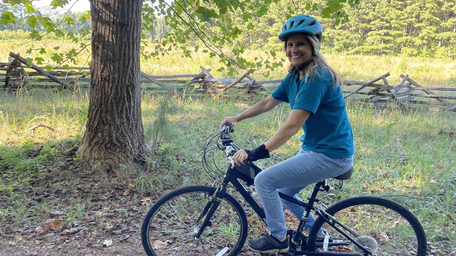 Woman with blue shirt and blue helmet riding a bike in the woods