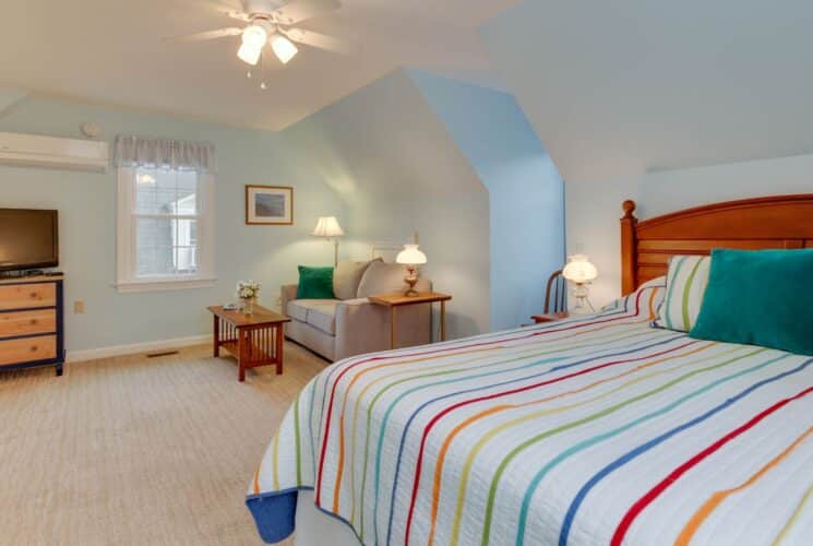 Suite with light blue walls, carpeting, wood headboard, multicolored striped bedding, light gray upholstered sofa, wood coffee table, and flatscreen TV