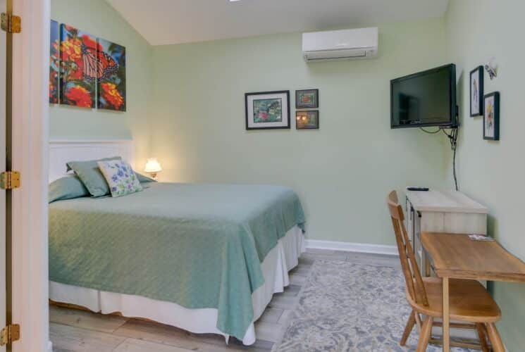 Bedroom with light green walls, hardwood flooring, light green bedding, wood desk and chair, and flatscreen TV