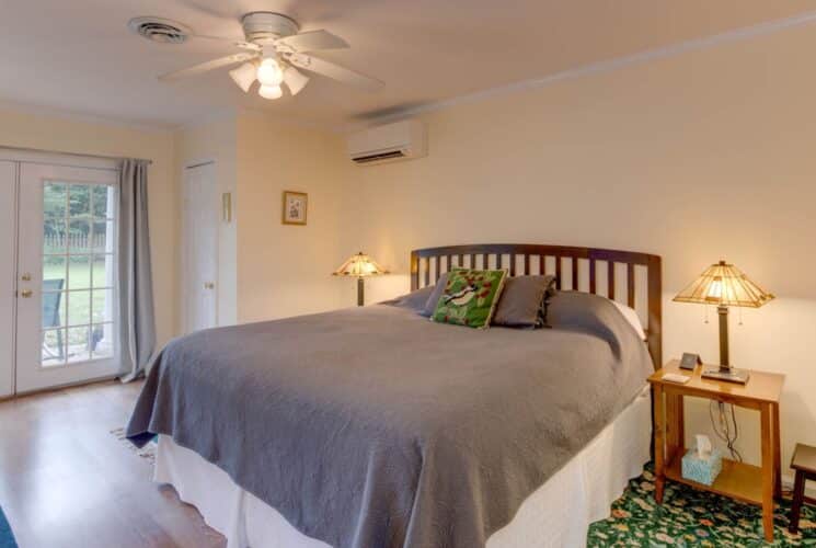 Suite with cream walls, hardwood flooring, wood headboard, gray bedding, and double doors to back patio