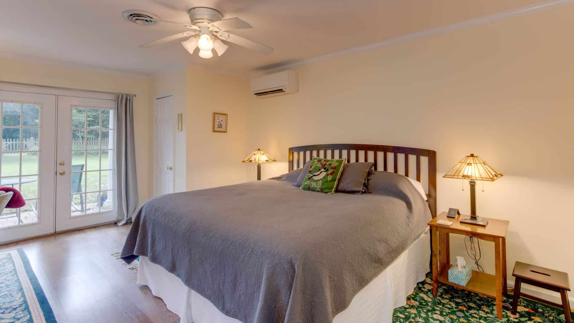 Suite with cream walls, hardwood flooring, wood headboard, gray bedding, and double doors to back patio