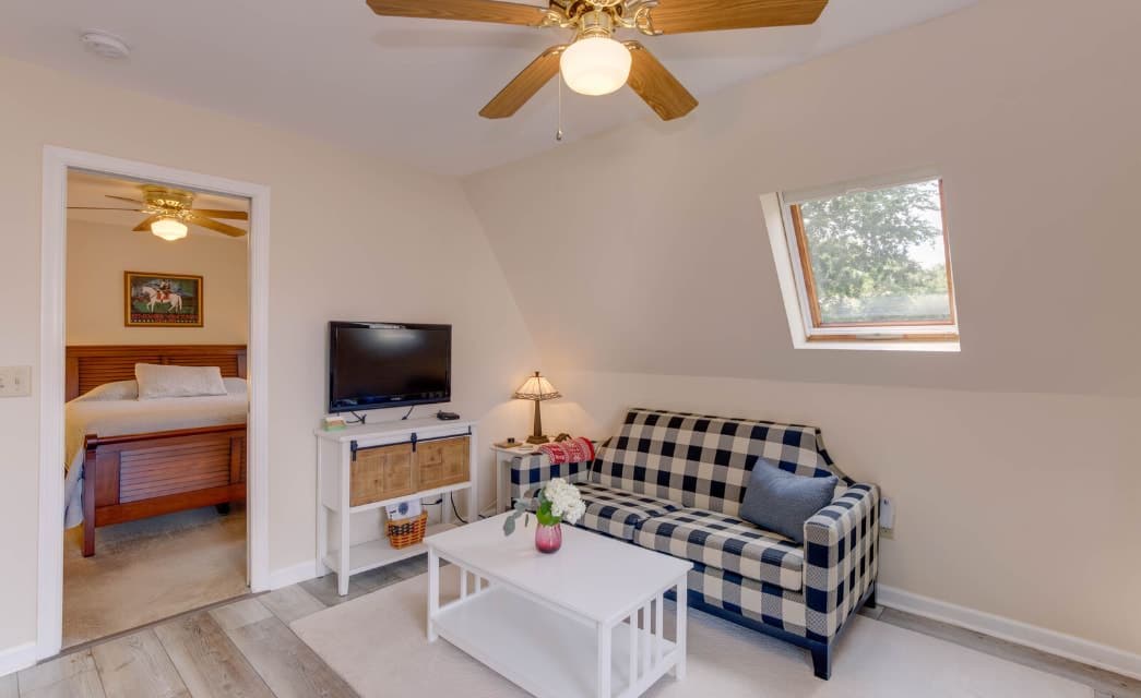 Living room with light colored walls, hardwood flooring, navy and white checked upholstered sofa, white coffee table, flatscreen TV, and view into bedroom