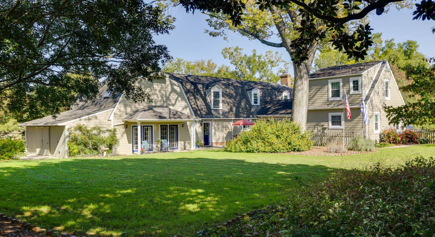 Exterior view of the property painted light taupe with white trim surrounded by green grass, green vegetation and large trees